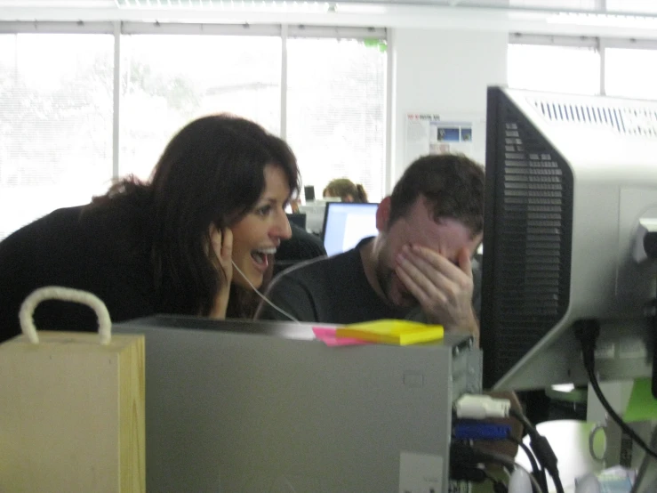 a man and woman look at a computer monitor while a boy covers his mouth