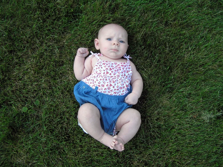 a small baby in a colorful top is on some grass