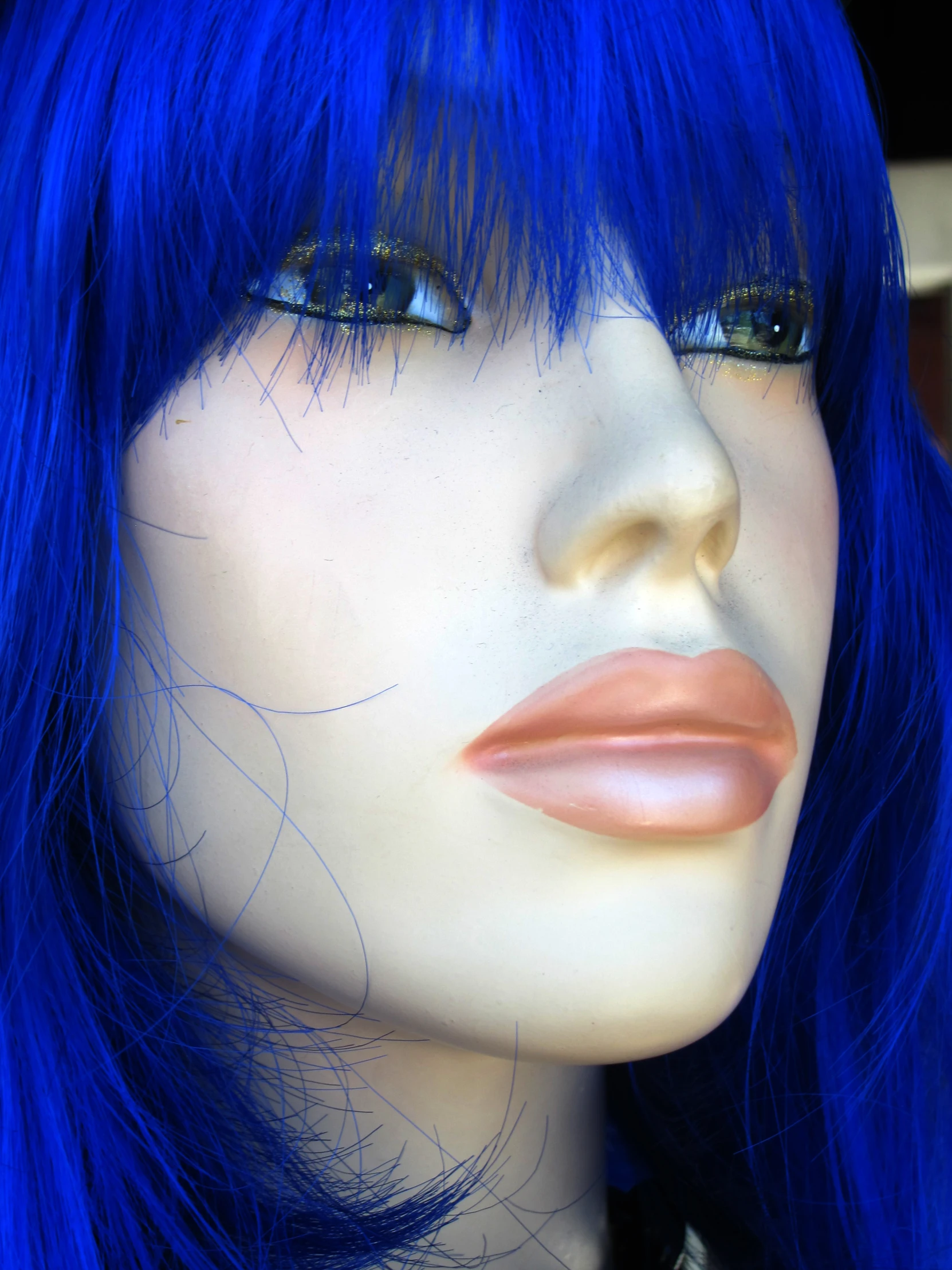 a white mannequin head and blue hair with orange and brown eyeliner