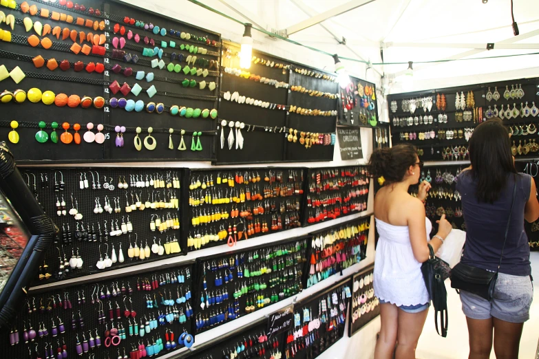 a woman looks at a display of a pair of young women in front of a store display with earring displays