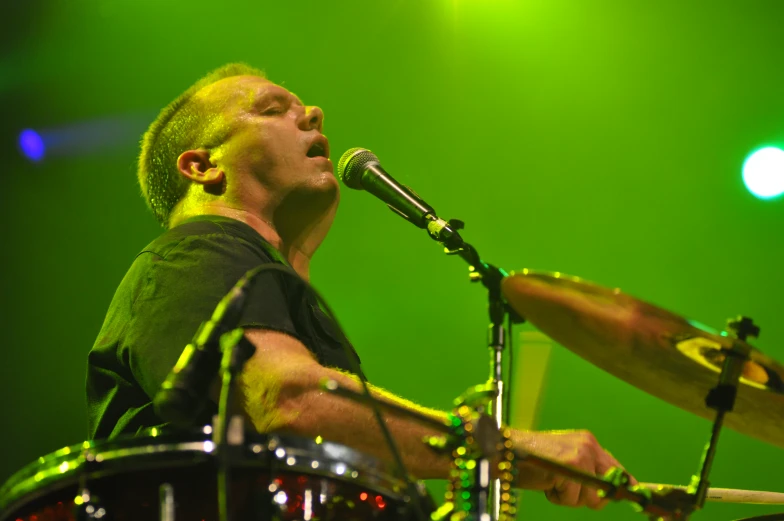 a man that is playing the drums and singing into some microphones