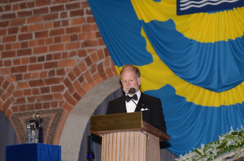 a man wearing a tuxedo stands at a podium