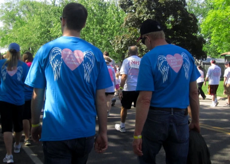 several men wearing blue shirts with hearts on their chests and one man wearing blue shirt has his back towards another in a city