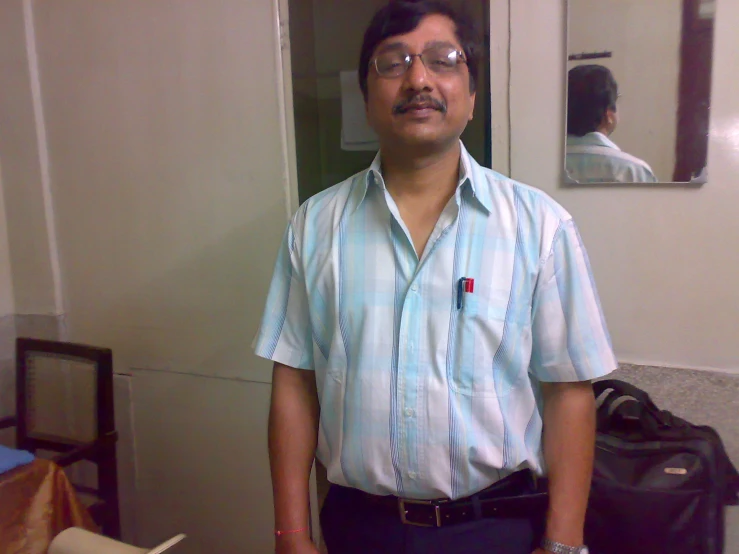 man with glasses standing next to a suitcase in front of a mirror