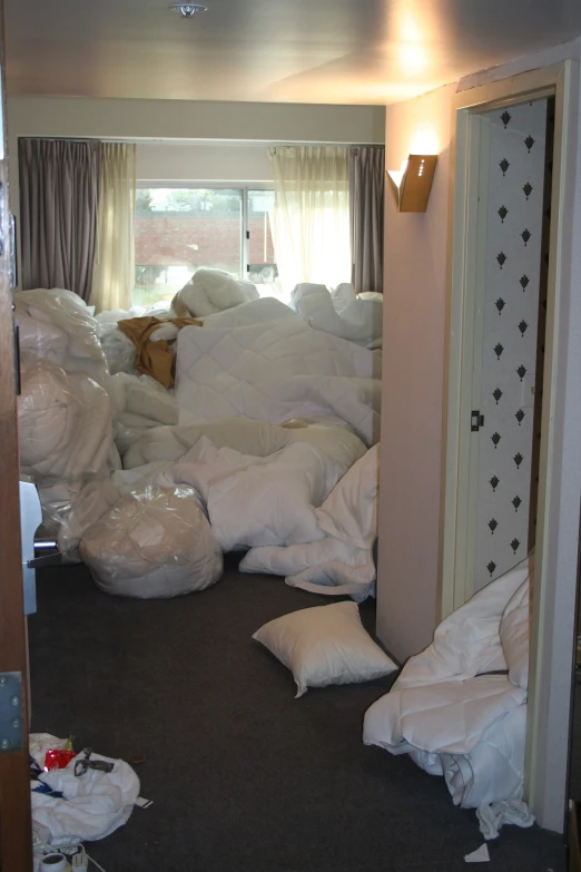 a bedroom with lots of unmade mattresses and dust bags piled on the floor