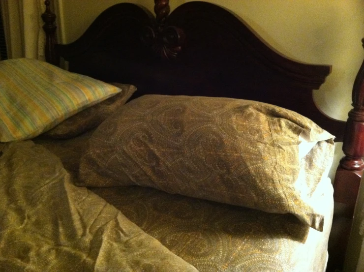 an unmade bed with a wooden headboard and a brown colored quilted comforter