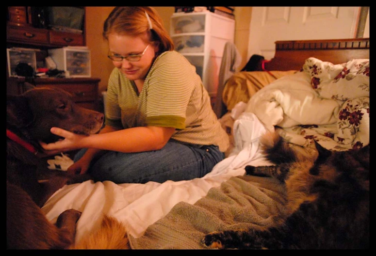 a woman sits on a bed with two dogs and cat