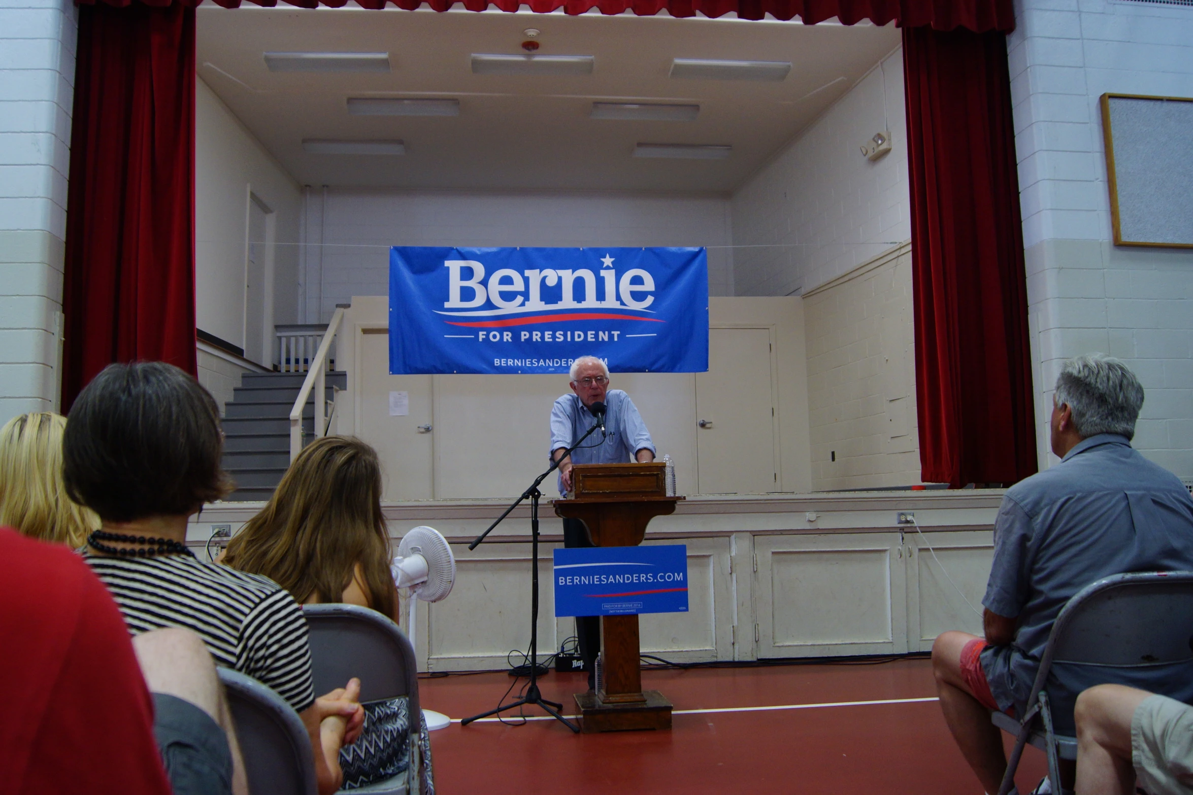 man on podium in auditorium with banner over stage