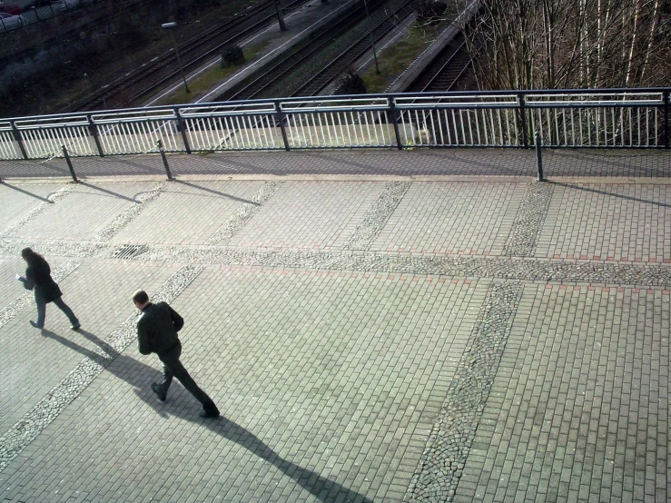 two people walking around in the sun on some pavement