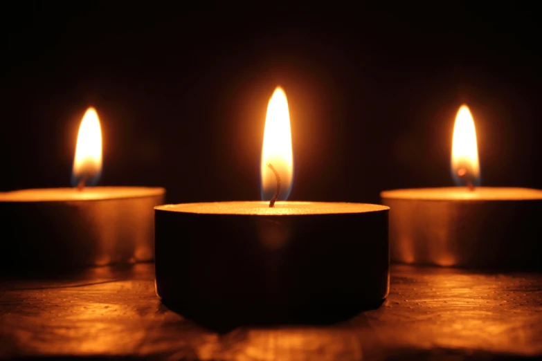 three lit candles with their reflections in the background