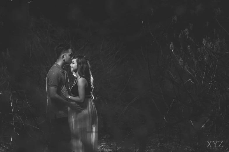 a couple holding each other standing next to each other in the dark forest