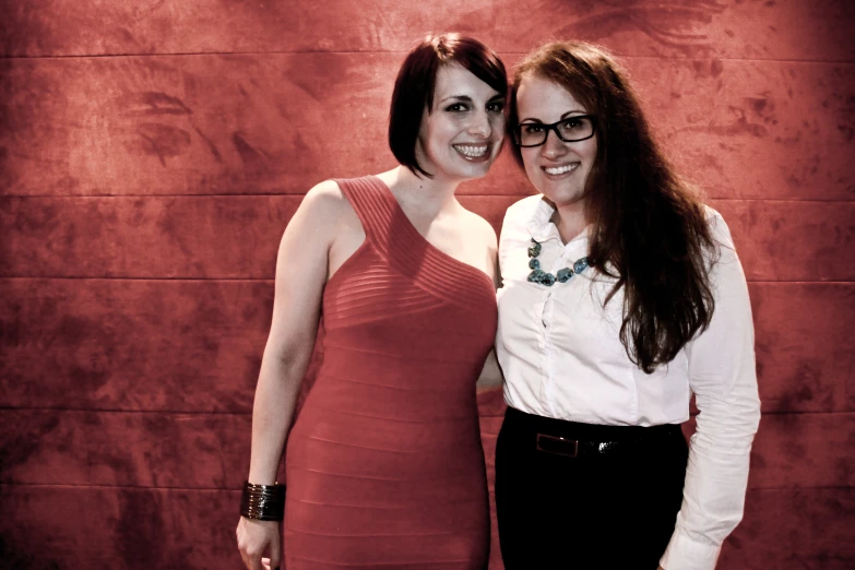 two ladies posing together in front of a red wall