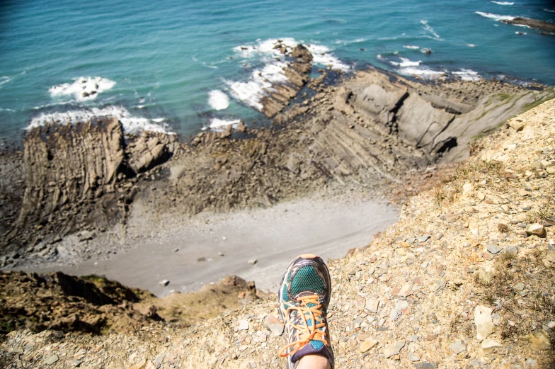 there is a person's feet on the edge of a cliff overlooking a beach