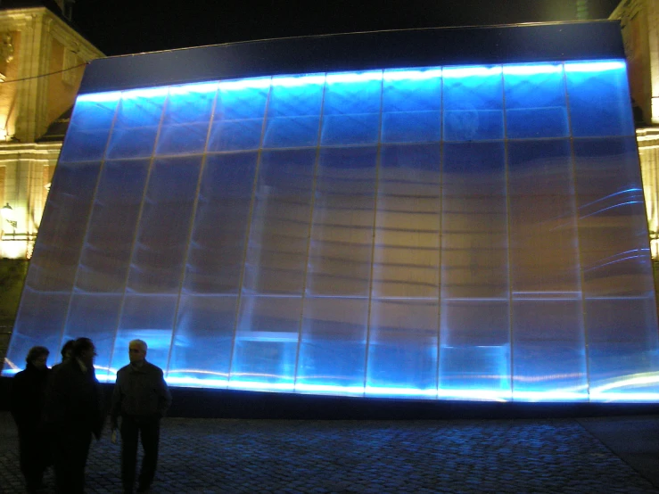 some people standing outside by a bright lit wall