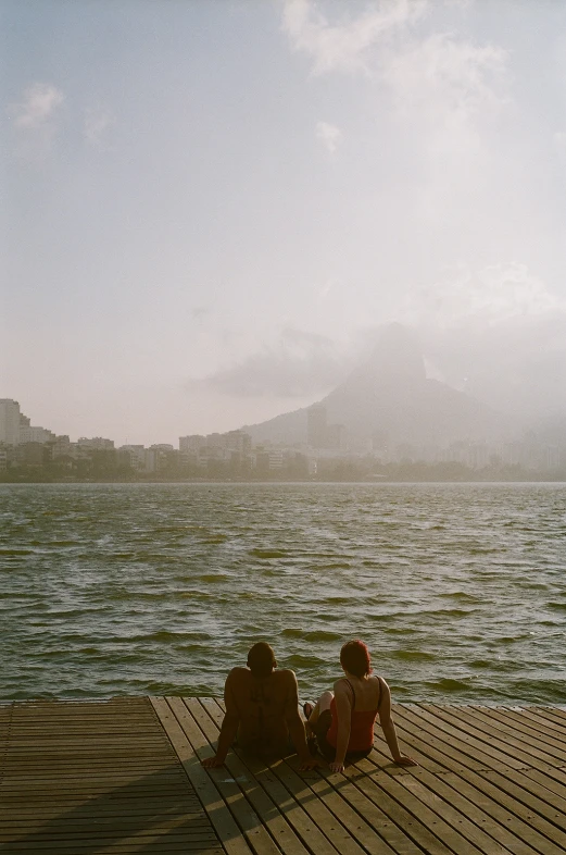 two people sit on a dock with the ocean in the background