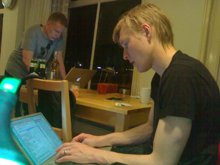 two men are at a table, one of them typing on his lap top