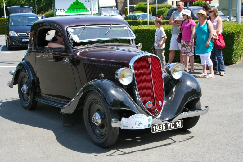 an old time car sits on the side of the road in front of a crowd