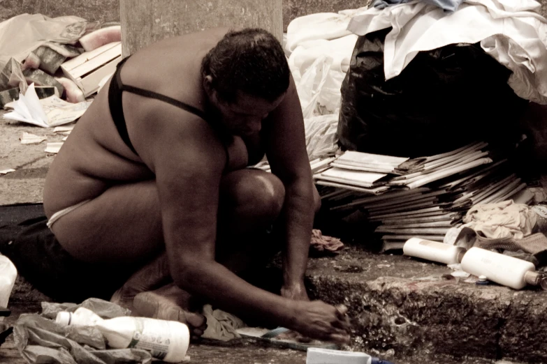 a man is squatted next to an open toilet on the ground