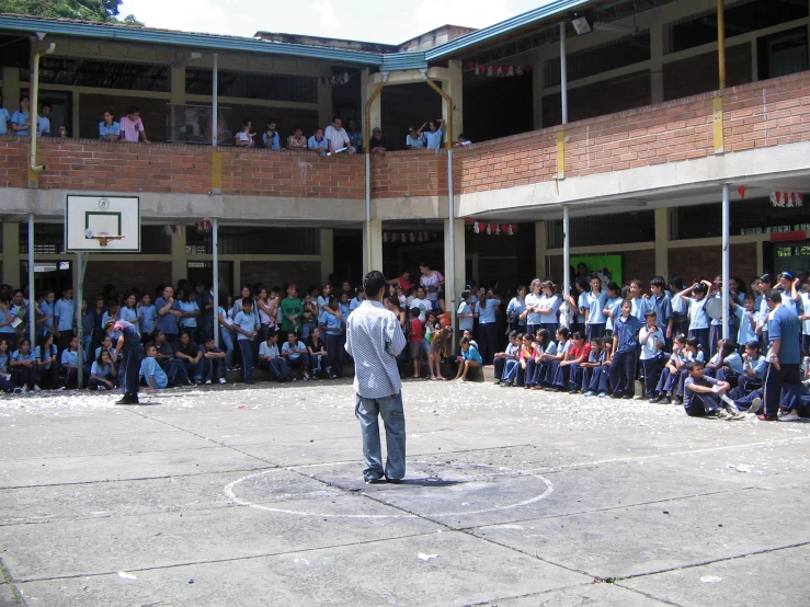 people in school uniforms watch one guy juggling at a basketball court