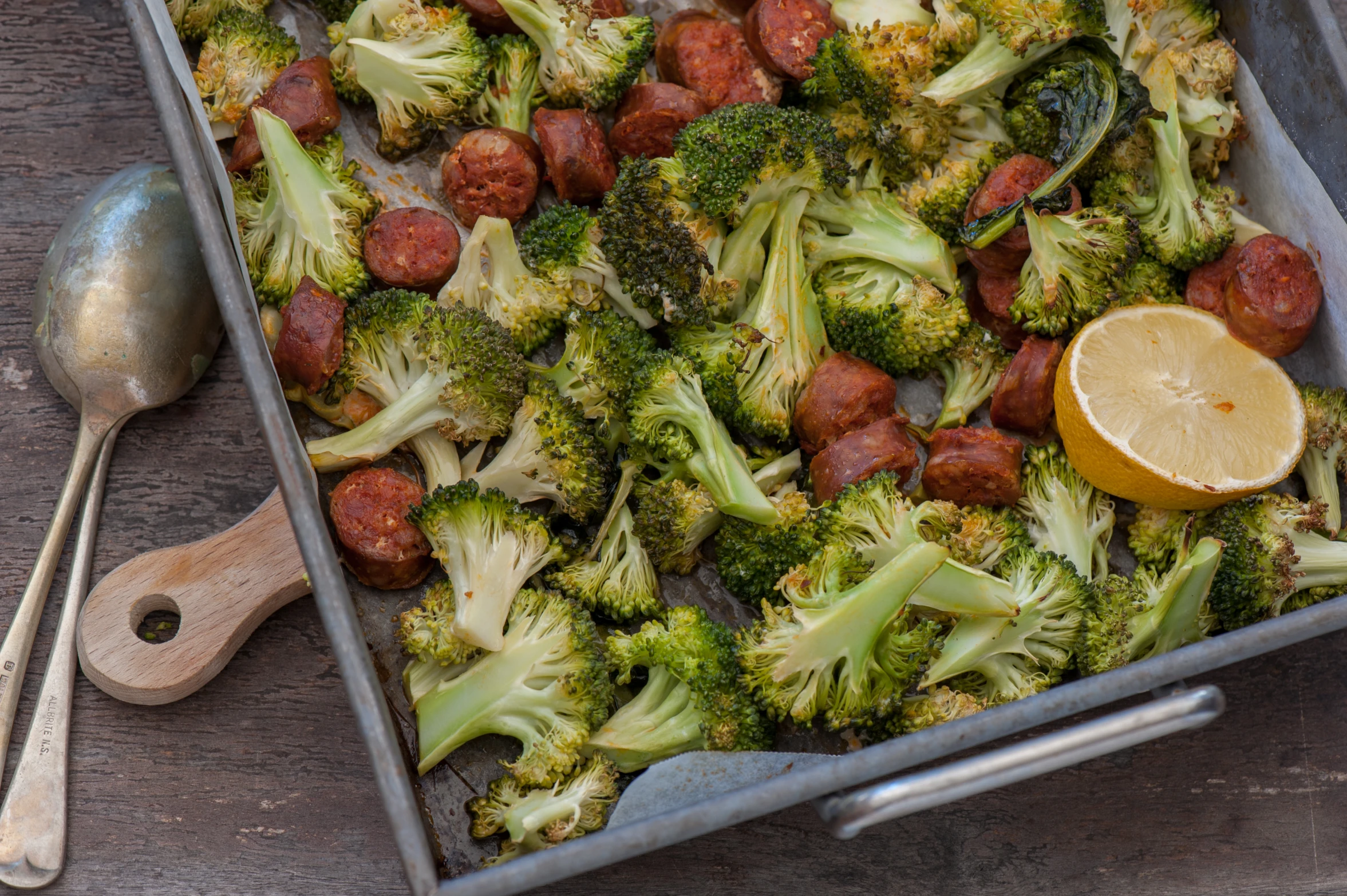 a tray filled with broccoli next to two spoons