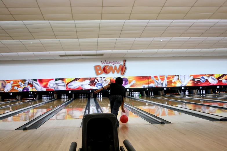 the young man is walking along bowling lanes holding his bowling ball