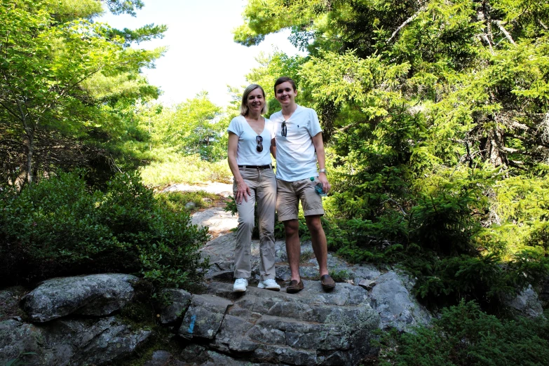 two people standing on a rock surrounded by green trees