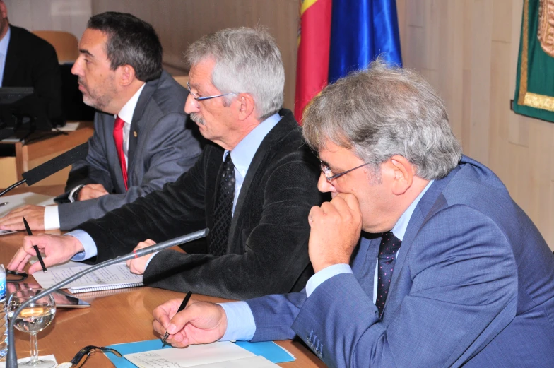 four men in suits and ties sit at a wooden table