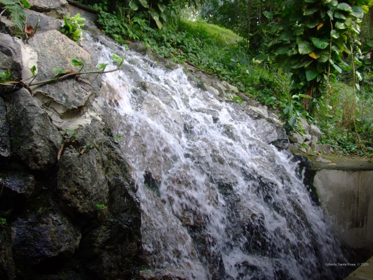 a large waterfall near rocks with trees in the background