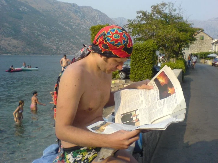 a person sitting by some water reading a paper