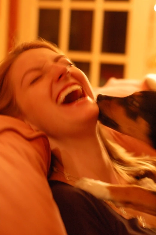 a woman smiles and laughs with her dog in front of a fireplace