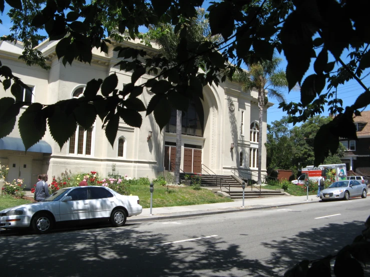 two cars parked outside a big, white building with stairs and landscaping