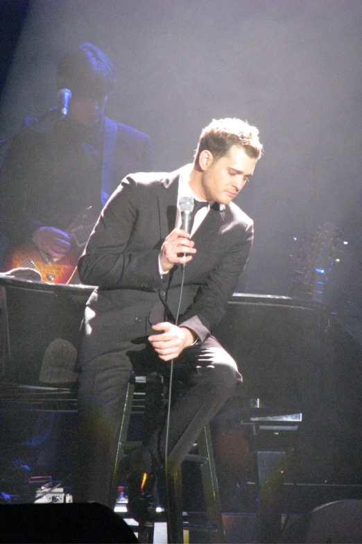 a man in a tuxedo sits on a chair with a microphone