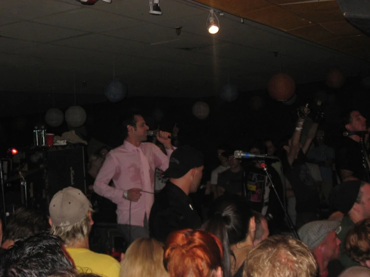 a man in pink shirt and jeans singing on stage