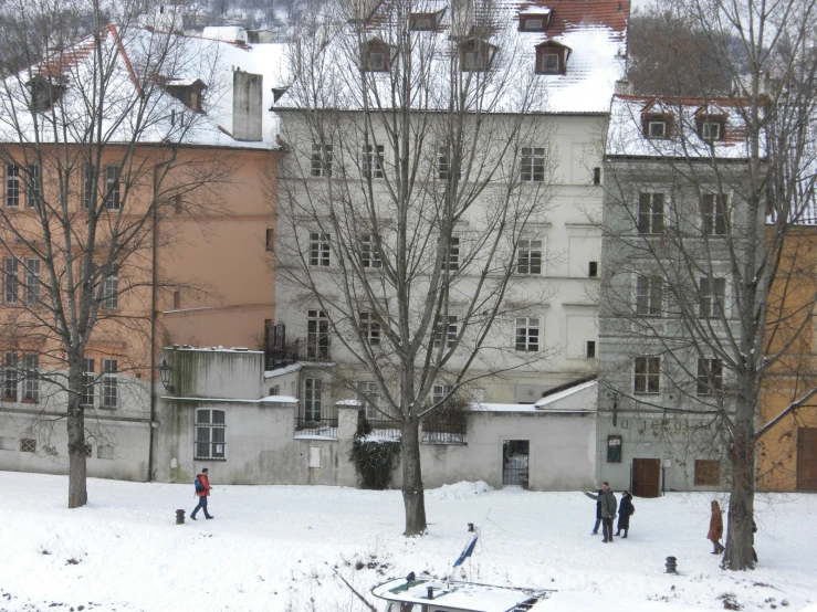 a group of people walking through the snow in front of some buildings