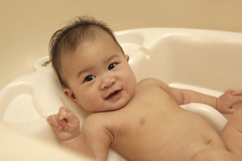 an infant is lying in a white bathtub with a smile