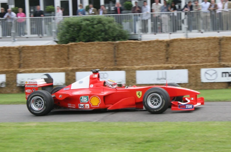 a red race car drives down a road by a large crowd