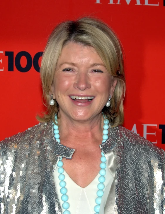 a smiling woman wearing a silver jacket and blue beads