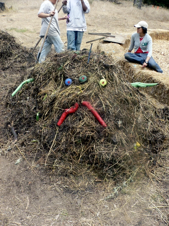 people standing around a pile of hay with some gardening tools