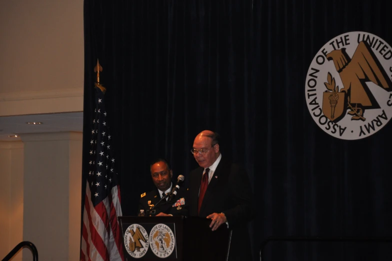 two men in suits speaking from behind a podium