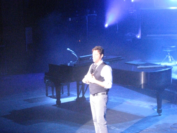 man on stage speaking into microphone and holding microphone to chest