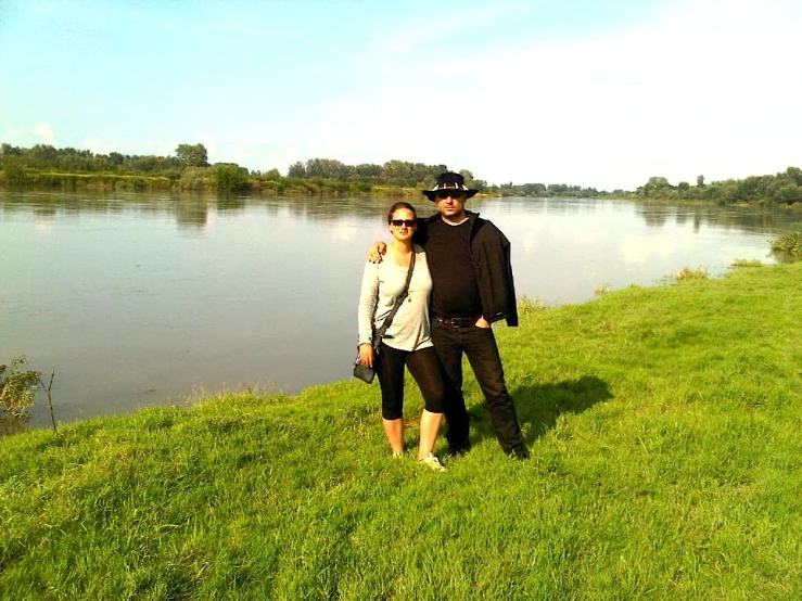 two people on the grass near water posing for a po