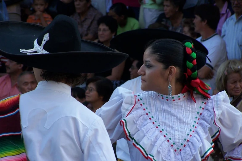a  wearing a mexican style dress and a man wearing a long dress in front of a crowd