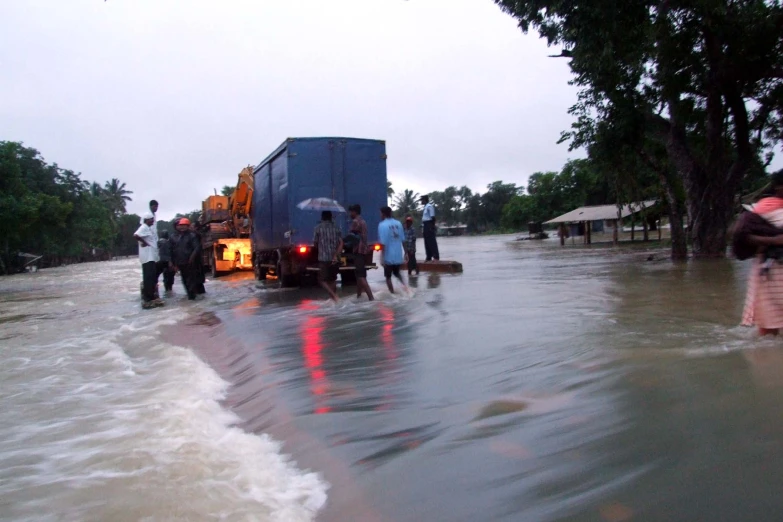 people standing in the water, moving their belongings through a flooded street