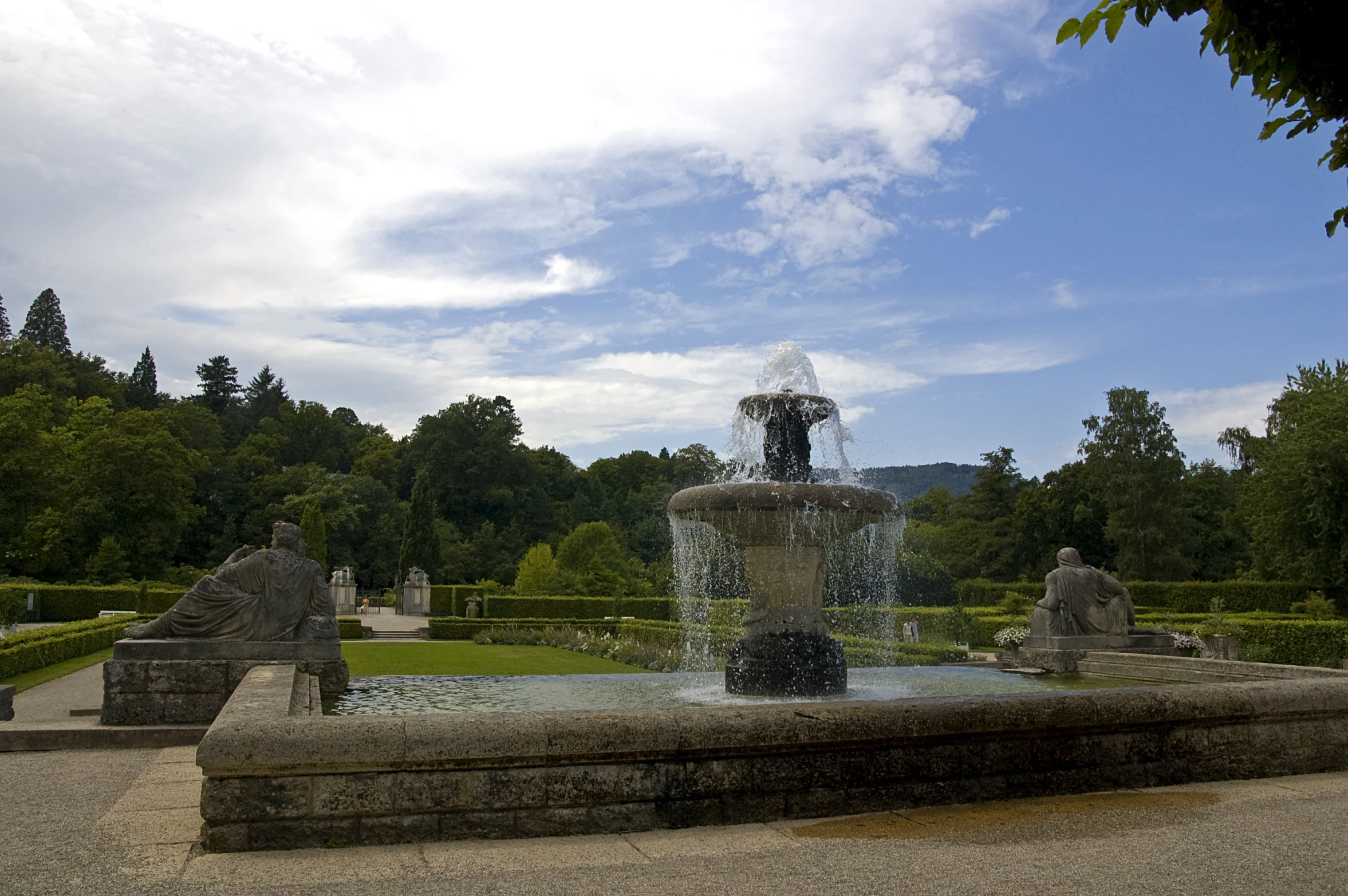 a large outdoor fountain is near many hedges