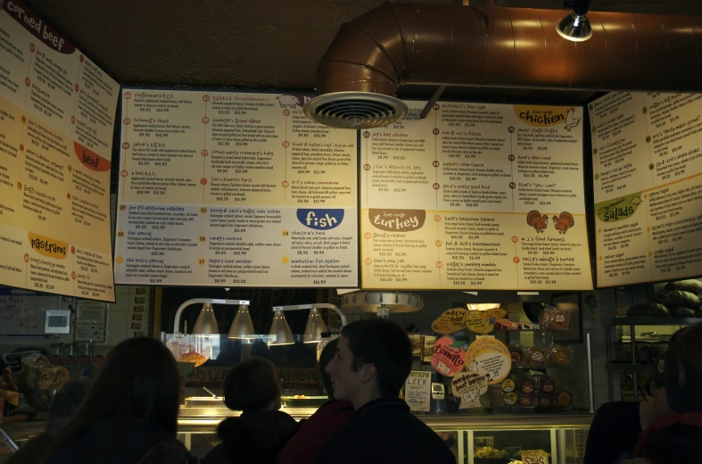 some people standing under a food court menu