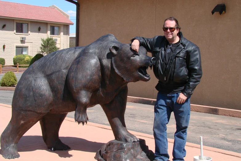 the man is posing with his large statue of a bear