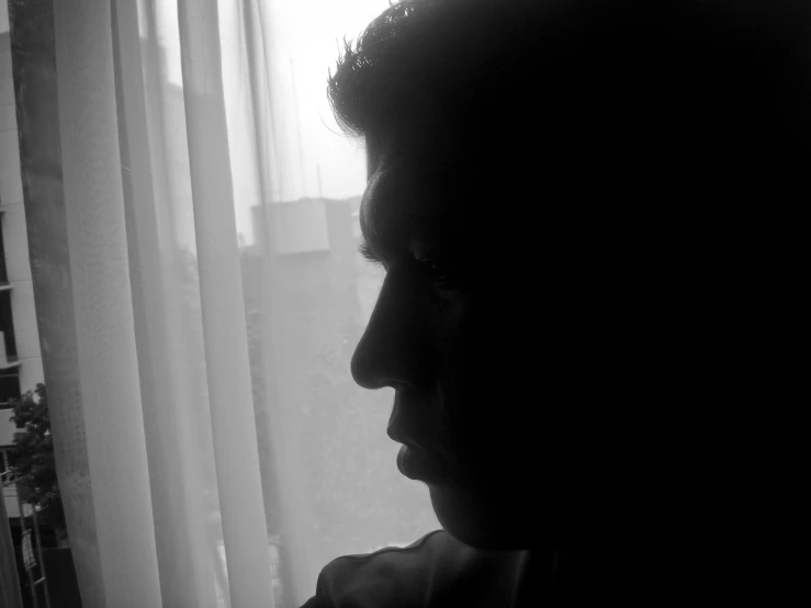 silhouette of a man next to a window with white curtains