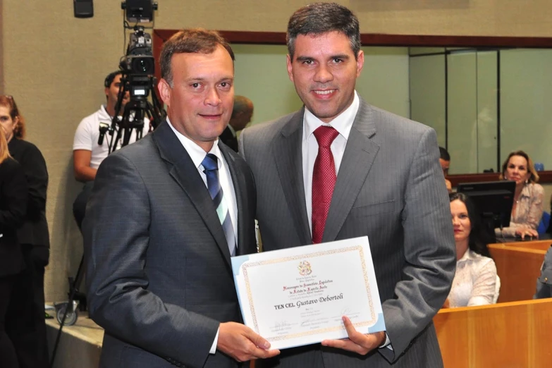 two men standing in an auditorium holding up a large certificate