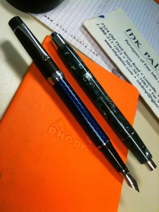 two pen sit next to each other on top of an orange notebook