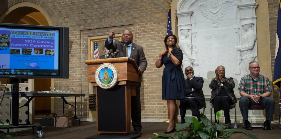 a man standing behind a podium with people watching